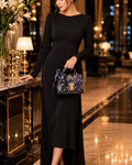 Woman in a black dress holding a patterned handbag in an elegant indoor setting.
