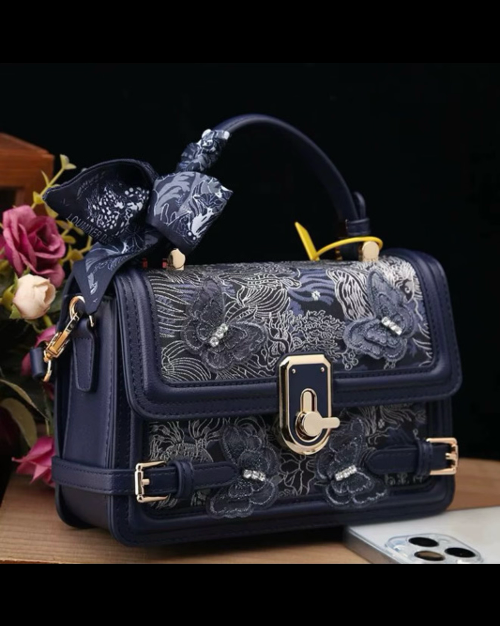 Navy blue handbag with floral lace design and gold accents on a dark background