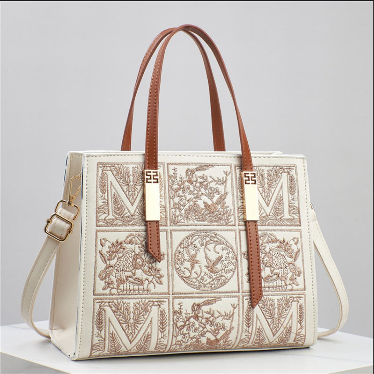 Designer handbag with intricate patterns and brown straps on a light gray background