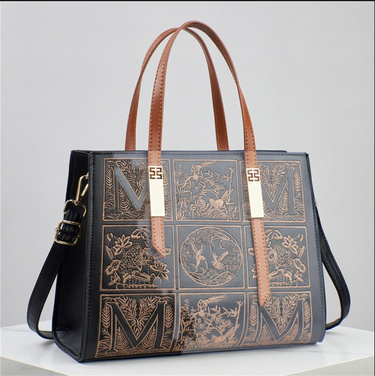 Designer handbag with embossed patterns and brown handles on a gray background