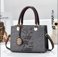 Gray handbag with floral embroidery and brown handles on a white surface.