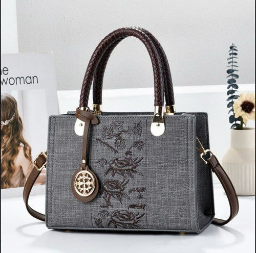 Gray handbag with floral embroidery and brown handles on a white surface.