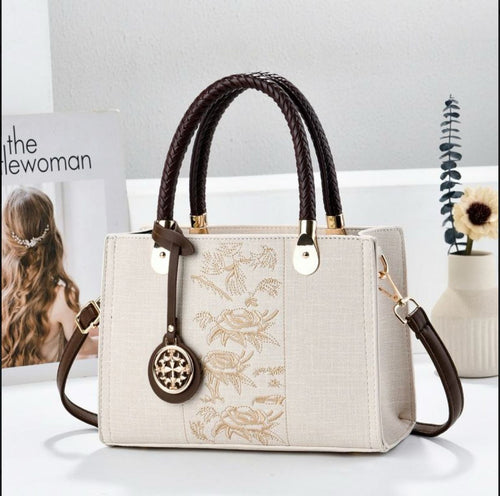 Handbag with floral embroidery and brown handles on a white surface