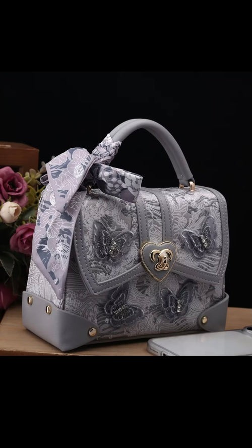 Gray handbag with floral design and heart-shaped clasp on a dark background