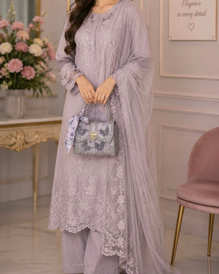 Woman in a light purple embroidered outfit holding a matching handbag in an elegant room.