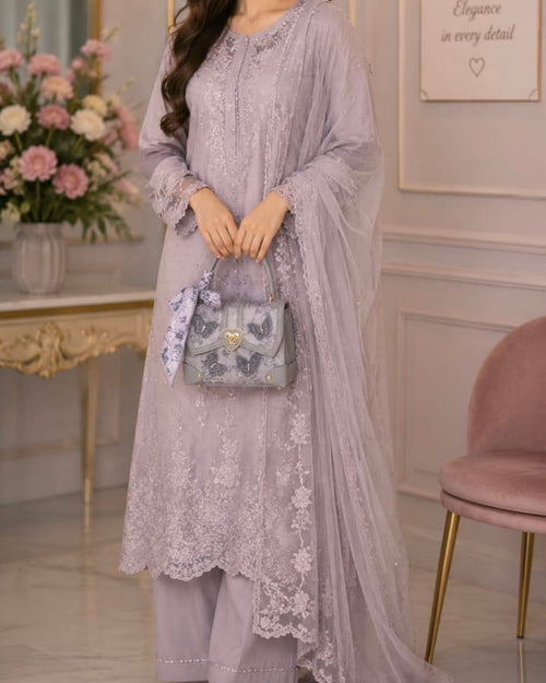 Woman in a light purple embroidered outfit holding a matching handbag in an elegant room.