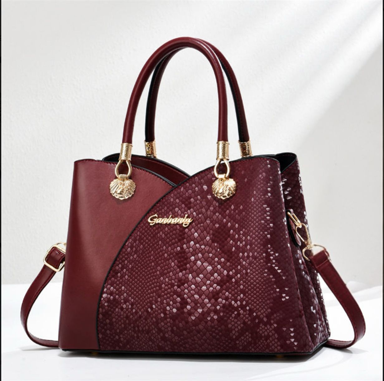 Burgundy handbag with gold accents on a white background
