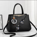 Black handbag with floral embroidery and a pom-pom charm on a white background