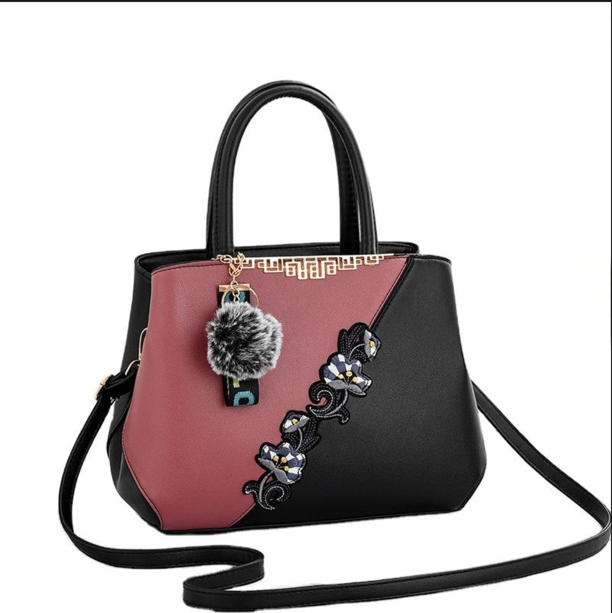 Two-toned handbag with floral design and pom-pom charm on a white background
