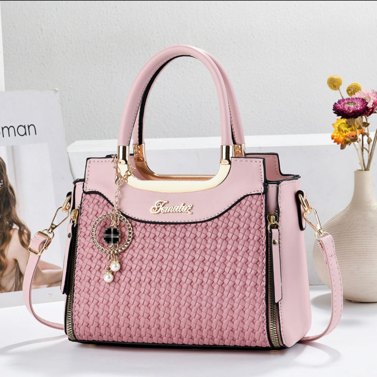 Pink handbag with gold accents on a white surface with a magazine and vase in the background
